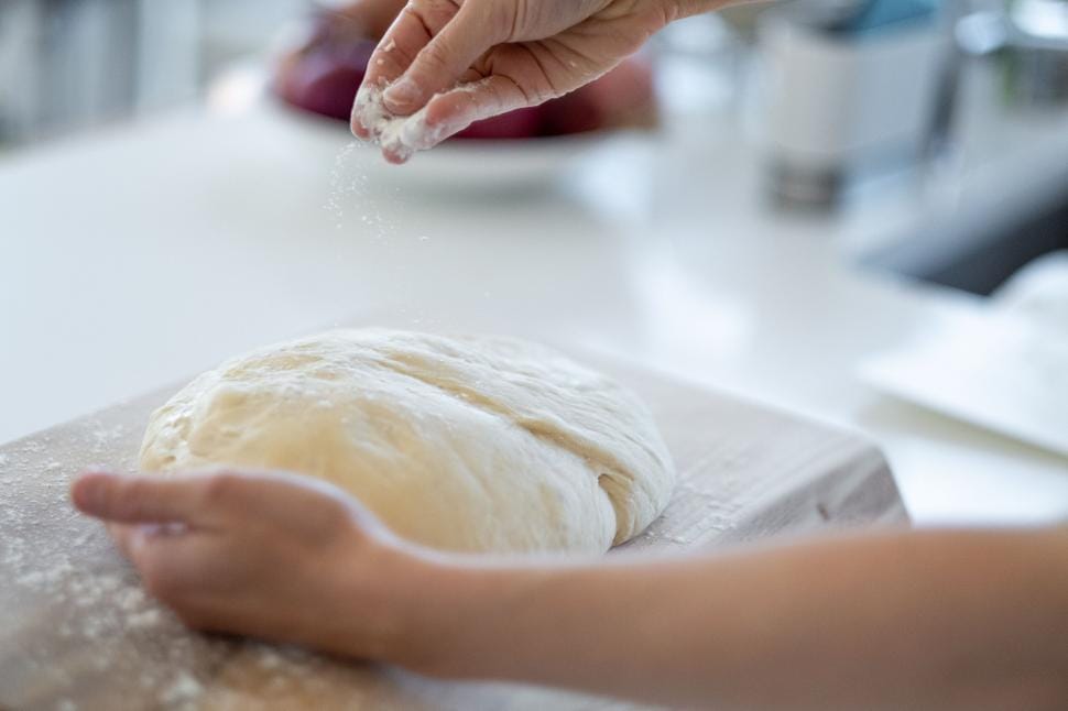 Baker's hands kneading dough on a flour-dusted bench